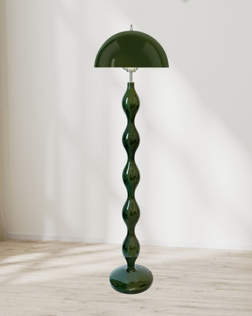Wavy green floor lamp with a painted metal dome shade and sculptural metal body, standing in a minimalist space with natural light.