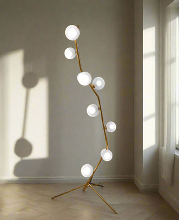 Sculptural floor lamp with a gold-painted metal body and frosted glass globes, featuring a branching design that casts dramatic shadows in a sunlit room.