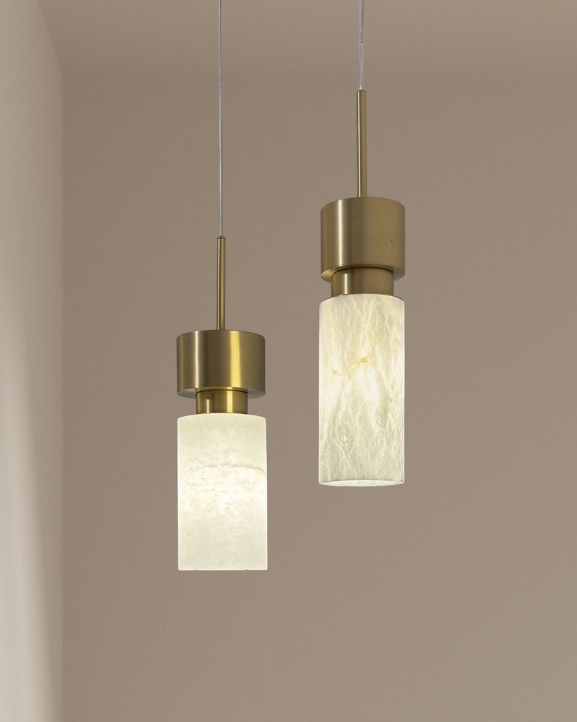 Pair of vertical alabaster pendant lights with iron brass finish hanging against a warm beige wall