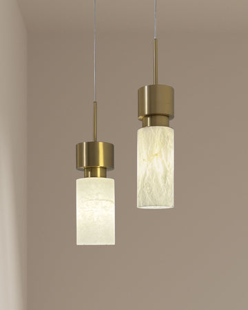 Pair of vertical alabaster pendant lights with iron brass finish hanging against a warm beige wall