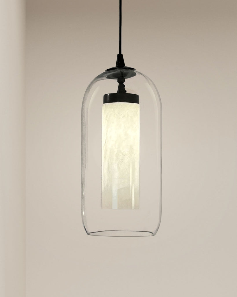 Modern alabaster cylinder pendant light with clear dome glass shade hanging against beige wall