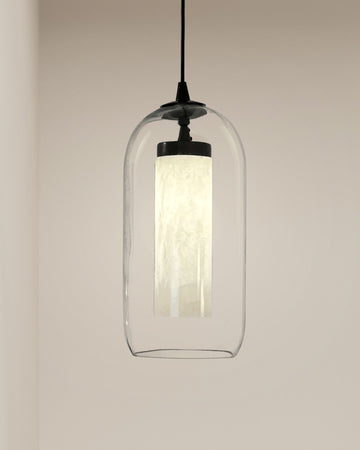 Modern alabaster cylinder pendant light with clear dome glass shade hanging against beige wall