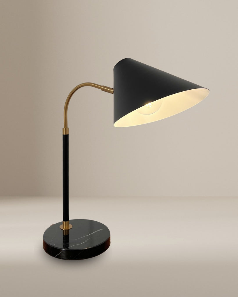 A modern black table lamp with a conical shade, brass neck, and circular black marble base, styled against a neutral background for a minimalist aesthetic.