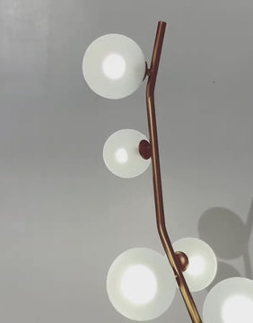Close-up of the Feliz floor lamp showing its gold-painted metal body and frosted glass globes against a clean white wall.