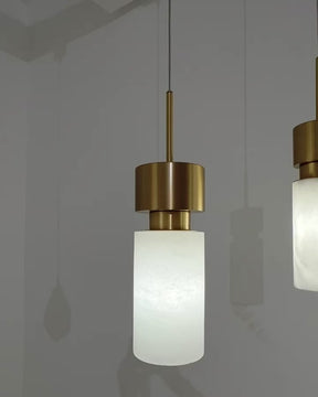 Close-up of two Auclair alabaster pendant lights with brushed iron brass finish, softly glowing against a light wall—perfect for elegant and modern interiors.