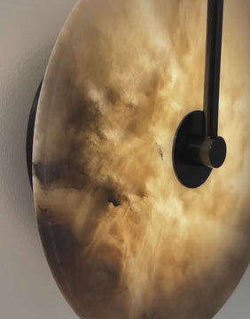 Modern round alabaster wall sconce with black loop arm glowing warmly against a light gray wall