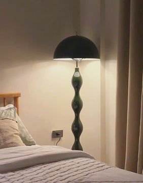 Green sculptural metal floor lamp softly illuminating a cozy bedroom corner beside a bed with neutral linens and curtains.