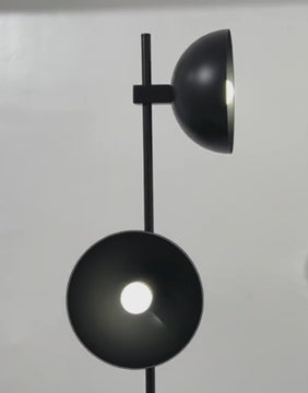 A close-up video of the Olav floor lamp’s twin black dome heads glowing softly against a white wall.