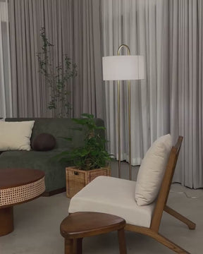 Modern gold floor lamp with fabric shade and marble base, placed beside green velvet sofa and indoor plant in a Japandi-style living room.